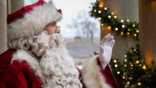 Close up of Father Christmas smiling and waving, Christmas decorations in the background.